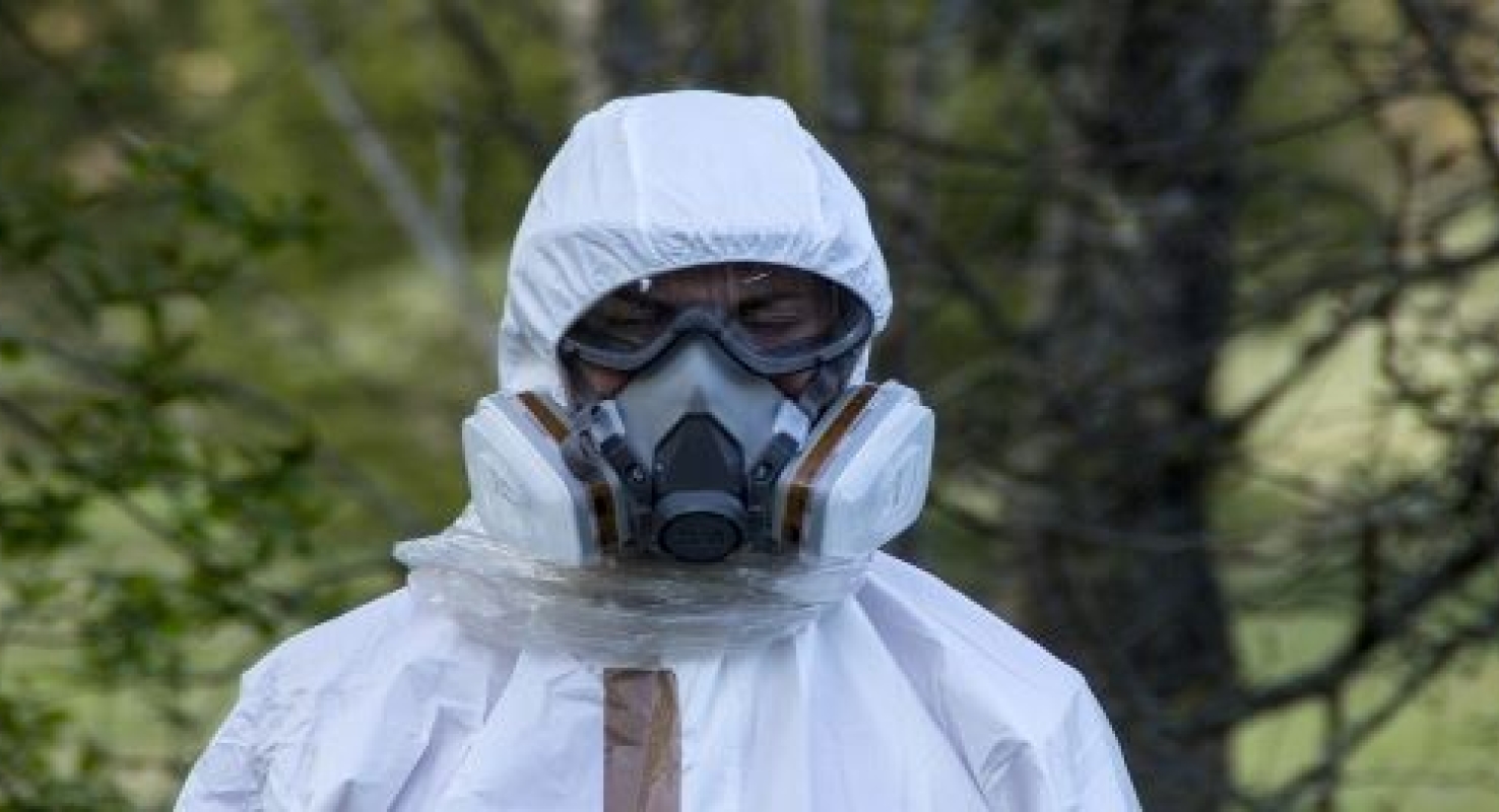 Een asbestsaneerder draagt een witte overall en een asbestmasker